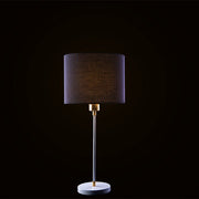 A black and white table lamp with a cylindrical shade, standing on a round base, with a visible gold accent at the top where the cord connects.